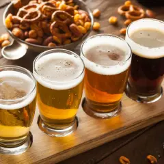 Quatre verres de bière, du plus clair au plus foncé, sur un plateau en bois, accompagnés de bretzels et de cacahuètes pour contrebalancer l'amertume.