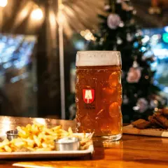 Bière ambrée dans un grand verre, accompagnée de frites et de croutons. L'ambiance festive suggère une recette bière de noël.