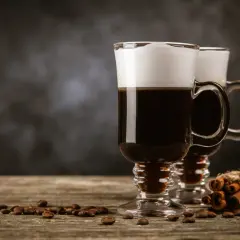 Deux cafés irlandais fumants, parfaits pour une recette irish réconfortante. Grains de café et bâtons de cannelle sur fond sombre.