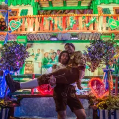 Ambiance de fête de la bière allemande : un homme porte un autre enlacé, entourés de décorations festives et de lumières vives.
