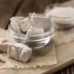 Blocs de levure fraîche périmée dans un bol en verre, prêts à être jetés. À côté, une autre coupelle contient de la levure sèche.