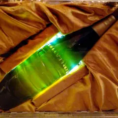 Une bouteille verte lumineuse, peut-être la bière la plus chère du monde, est présentée dans un écrin de tissu doré.