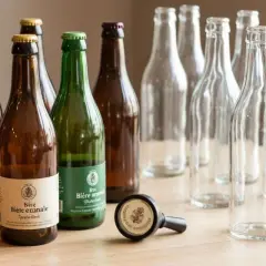 Bouteilles de bière non pasteurisée, certaines pleines, d'autres vides, sur une table en bois. Une liste de bières artisanales.