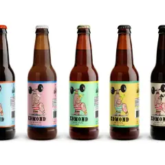 Cinq bouteilles de bière algérienne Edmond, aux étiquettes colorées représentant un haltérophile musclé.