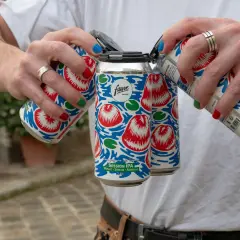 Main d'une personne aux ongles colorés manipulant des canettes de bière Fauve Session IPA.