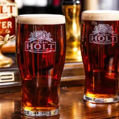 Deux verres de bière ambrée, une cask ale Joseph Holt, sur un comptoir en bois.