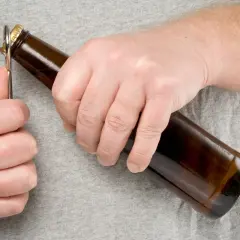 Main gauche ouvrant une bouteille de bière avec un décapsuleur. L'embouteillage bière est imminent.