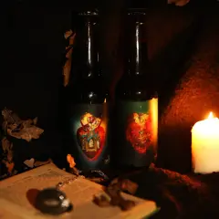 Deux bouteilles de bière la débauche 27 degré, éclairées par une bougie, entourées de feuilles mortes et d'un livre ouvert.