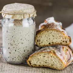 Un bocal de levain pétillant à côté de pains artisanaux coupés. Une invitation à remplacer levure par levain pour un goût authentique.