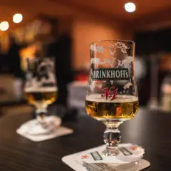 Deux verres de bières allemandes Brinkhoff's, l'un à moitié plein, sur une table sombre.