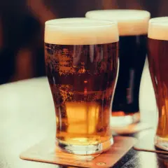 Trois verres de bière irlandaise connue, dont une stout foncée, sur une table.
