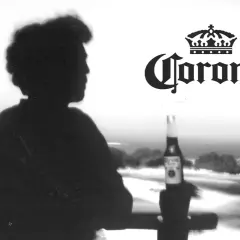 Silhouette d'une personne contemplant la mer, une bouteille de bière Corona à la main. L'image évoque l'origine de la bière Corona.