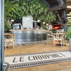Entrée de la brasserie française "Le Choupinet", décorée de verdure luxuriante et d'un bar moderne.