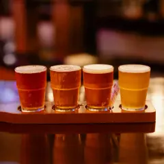 Quatre verres de bière, de différentes couleurs, sur un plateau en bois. Une dégustation de bière, pas de bière chaude ici !