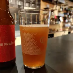 Bière artisanale "Crème Fraîche" dans un verre, avec une bouteille à côté. L'arôme subtil du houblon se marie à la douceur crémeuse.