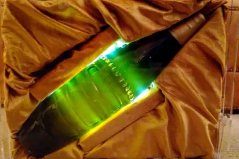 Une bouteille verte lumineuse, peut-être la bière la plus chère du monde, est présentée dans un écrin de tissu doré.