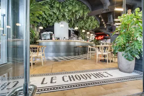 Entrée de la brasserie française "Le Choupinet", décorée de verdure luxuriante et d'un bar moderne.
