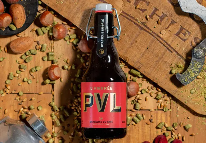 Bouteille de bière brune PVL, entourée de noisettes, de houblon et de grains. Une invitation à découvrir la recette biere brune.