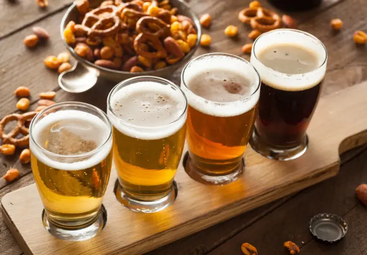 Quatre verres de bière, du plus clair au plus foncé, sur un plateau en bois, accompagnés de bretzels et de cacahuètes pour contrebalancer l'amertume.