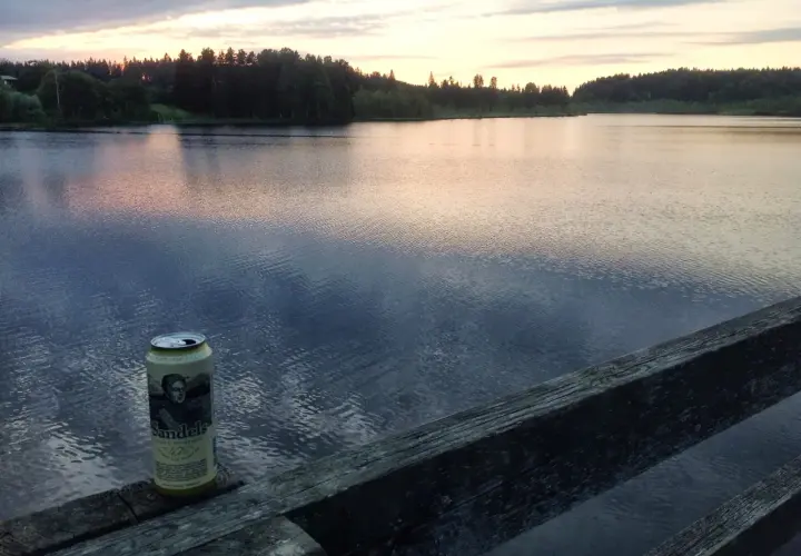 Une canette de bière Sandels, une bière karhu, repose sur un vieux bois au bord d'un lac paisible au coucher du soleil.