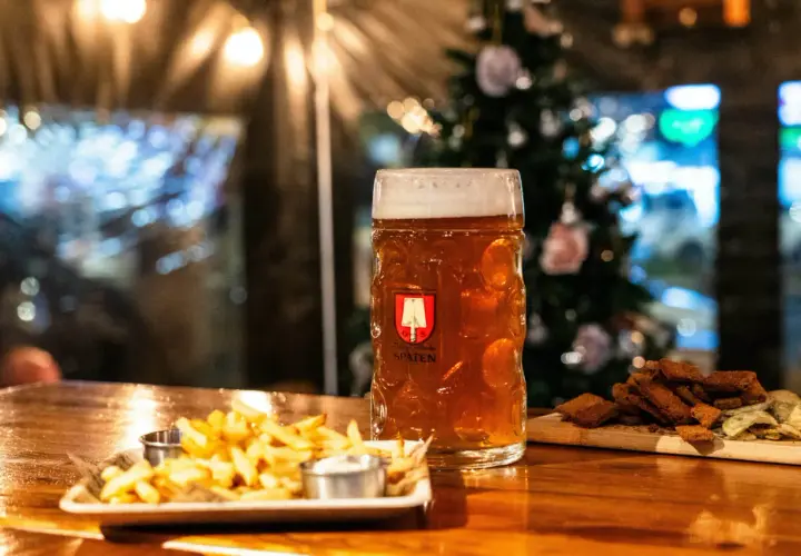 Bière ambrée dans un grand verre, accompagnée de frites et de croutons. L'ambiance festive suggère une recette bière de noël.
