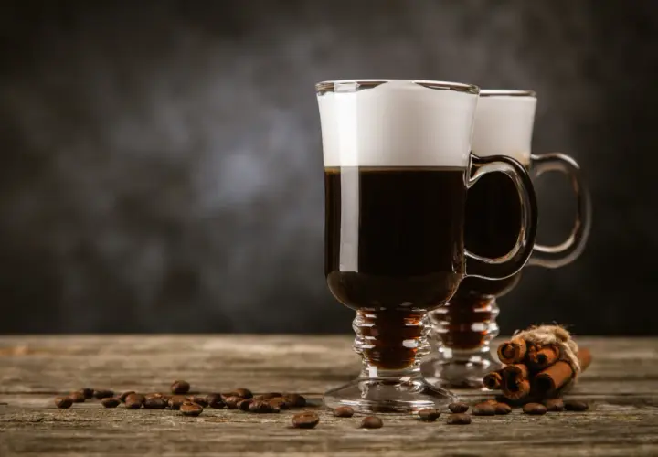 Deux cafés irlandais fumants, parfaits pour une recette irish réconfortante. Grains de café et bâtons de cannelle sur fond sombre.