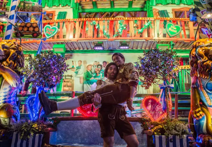 Ambiance de fête de la bière allemande : un homme porte un autre enlacé, entourés de décorations festives et de lumières vives.