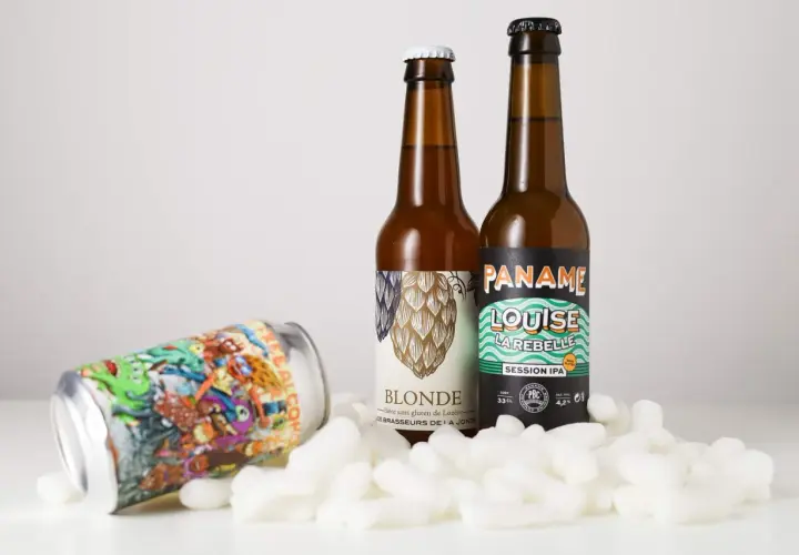 Deux bouteilles de bière et une canette colorée, dont une "Session IPA", reposent sur des flocons blancs.