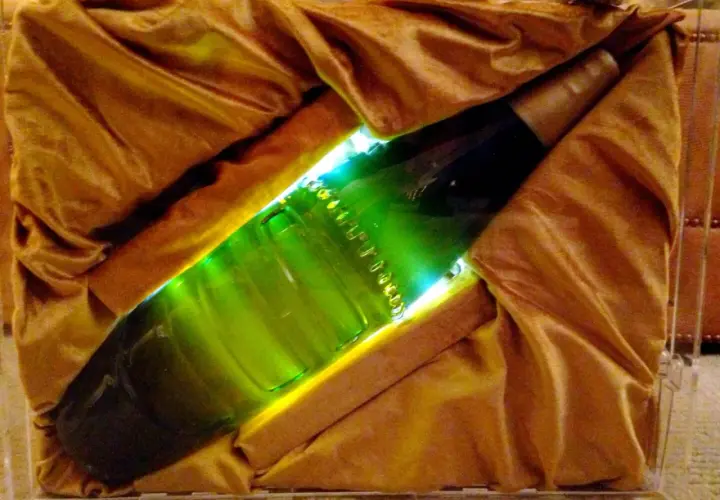 Une bouteille verte lumineuse, peut-être la bière la plus chère du monde, est présentée dans un écrin de tissu doré.