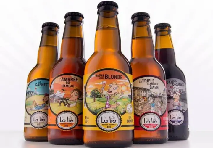 Cinq bouteilles de bière artisanale "La Lie", dont la meilleure bière normande. Des étiquettes colorées illustrent des scènes champêtres et urbaines.