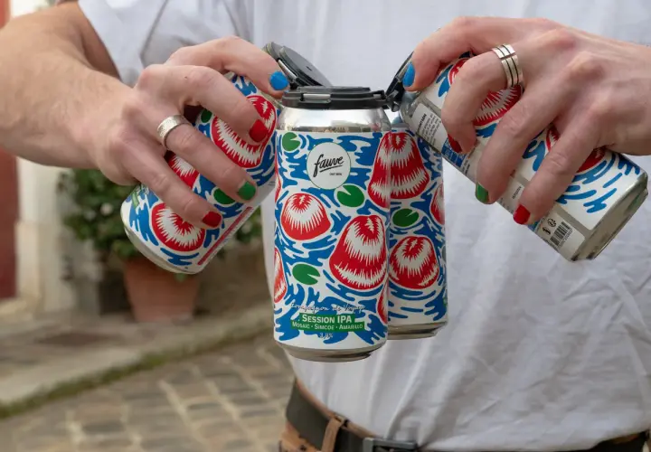 Main d'une personne aux ongles colorés manipulant des canettes de bière Fauve Session IPA.
