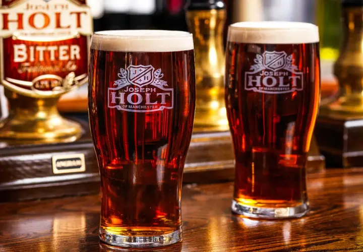 Deux verres de bière ambrée, une cask ale Joseph Holt, sur un comptoir en bois.