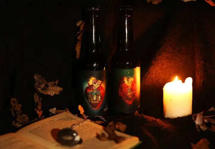 Deux bouteilles de bière la débauche 27 degré, éclairées par une bougie, entourées de feuilles mortes et d'un livre ouvert.