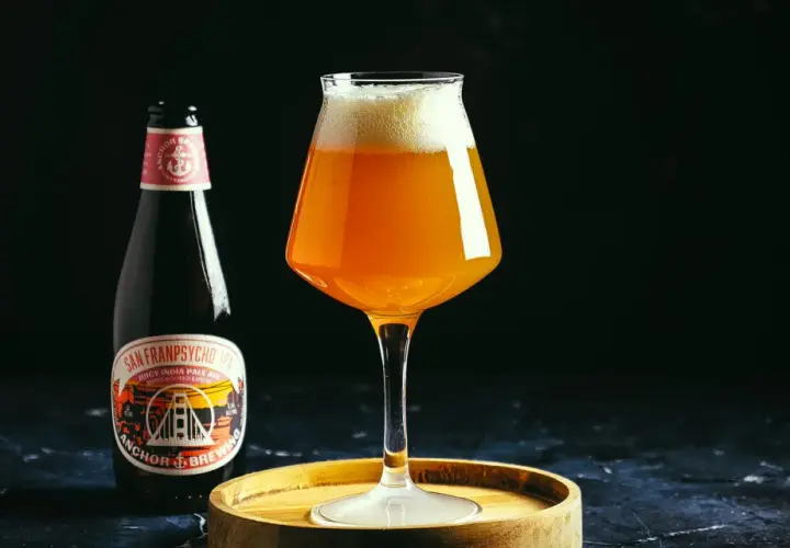 Une bouteille et un verre de bière ambrée Anchor, avec une mousse généreuse. L'étiquette de la bière mentionne "Anchor Brewing".