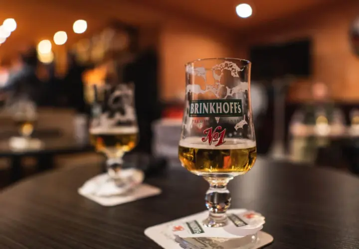 Deux verres de bières allemandes Brinkhoff's, l'un à moitié plein, sur une table sombre.