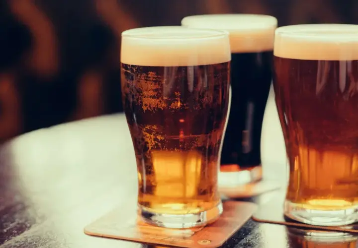 Trois verres de bière irlandaise connue, dont une stout foncée, sur une table.