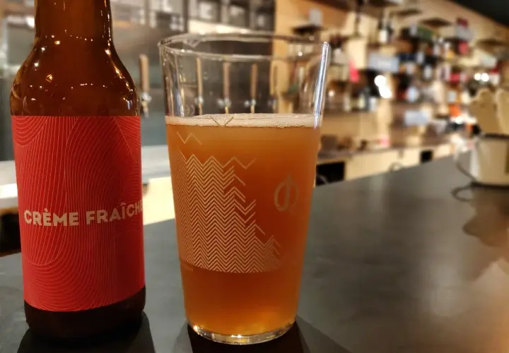 Bière artisanale "Crème Fraîche" dans un verre, avec une bouteille à côté. L'arôme subtil du houblon se marie à la douceur crémeuse.