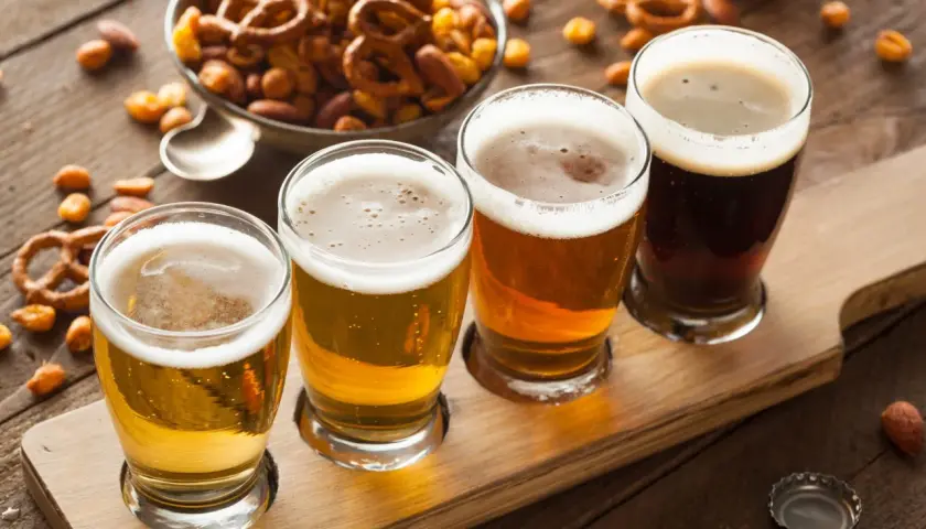 Quatre verres de bière, du plus clair au plus foncé, sur un plateau en bois, accompagnés de bretzels et de cacahuètes pour contrebalancer l'amertume.