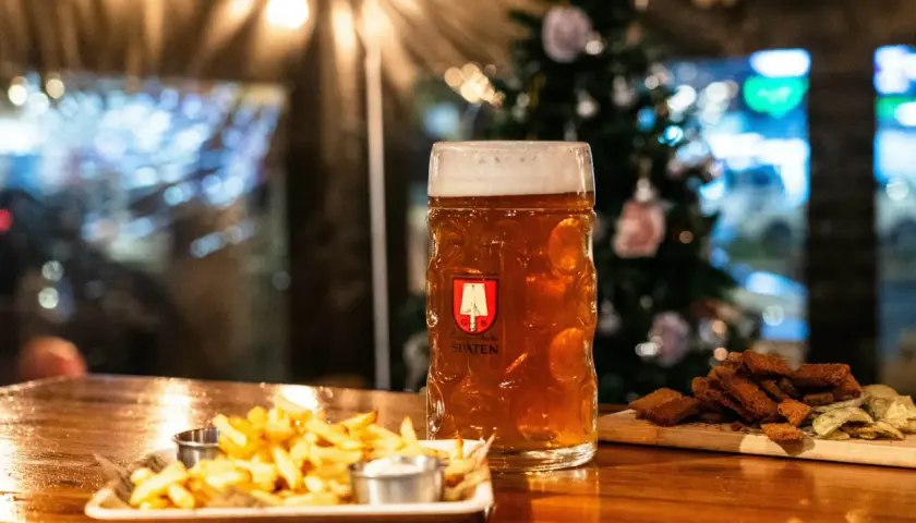 Bière ambrée dans un grand verre, accompagnée de frites et de croutons. L'ambiance festive suggère une recette bière de noël.