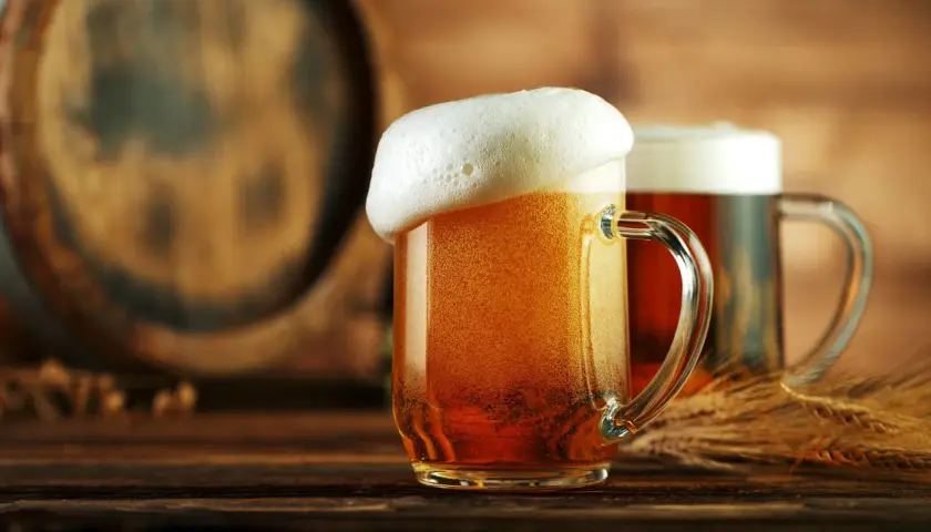 Deux chopes de bière dorée, mousseuse, près d'un tonneau. Une bière disparue, mais le plaisir reste.