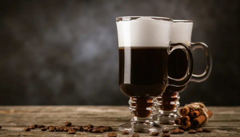 Deux cafés irlandais fumants, parfaits pour une recette irish réconfortante. Grains de café et bâtons de cannelle sur fond sombre.