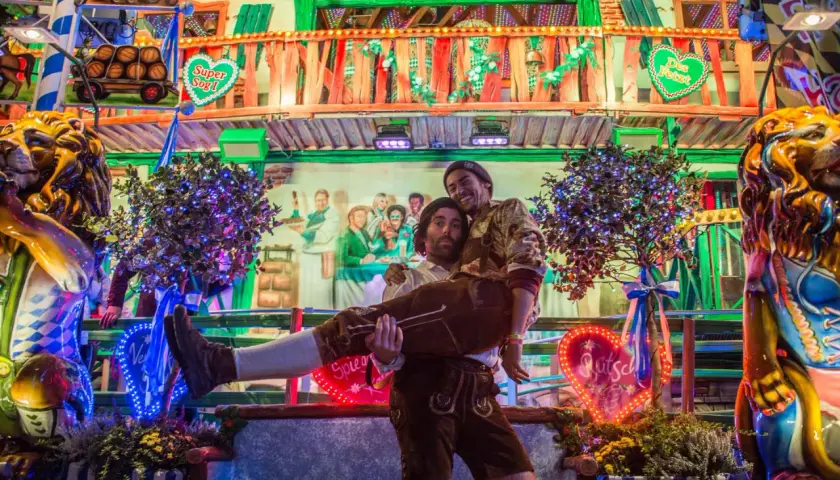 Ambiance de fête de la bière allemande : un homme porte un autre enlacé, entourés de décorations festives et de lumières vives.