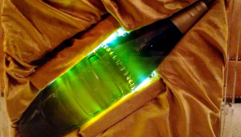 Une bouteille verte lumineuse, peut-être la bière la plus chère du monde, est présentée dans un écrin de tissu doré.
