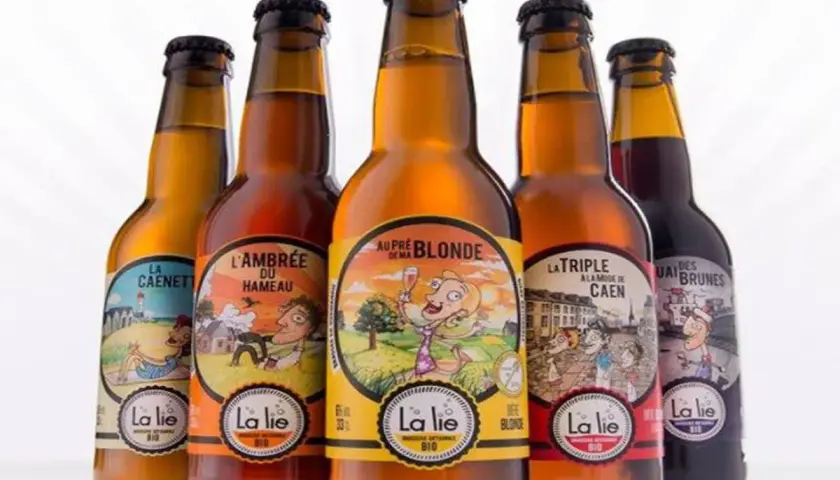 Cinq bouteilles de bière artisanale "La Lie", dont la meilleure bière normande. Des étiquettes colorées illustrent des scènes champêtres et urbaines.