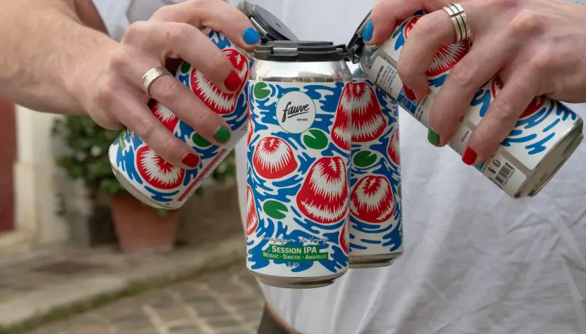 Main d'une personne aux ongles colorés manipulant des canettes de bière Fauve Session IPA.