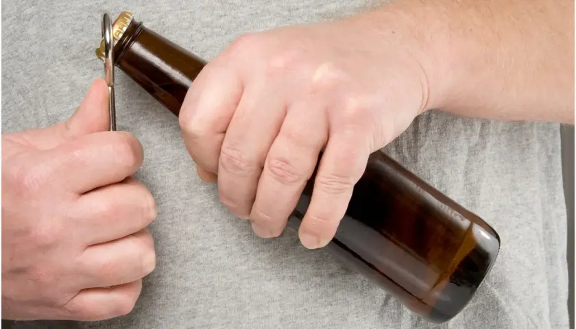 Main gauche ouvrant une bouteille de bière avec un décapsuleur. L'embouteillage bière est imminent.