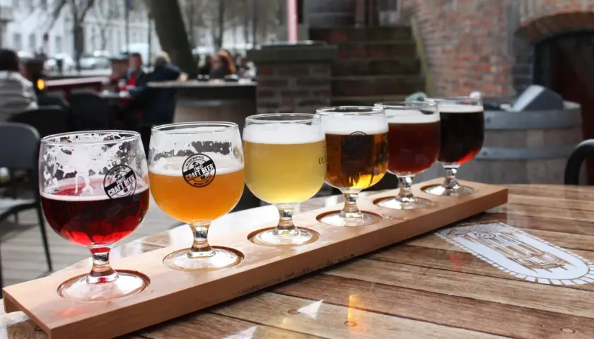 Dégustation de bières artisanales dans un bar. Cinq verres de différentes couleurs sur un plateau en bois.