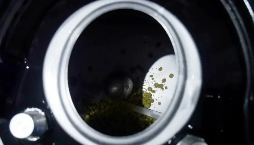Vue de dessus d'un récipient rempli de houblon. Des granulés verts, le houblon, sont visibles, certains tombant comme un "hop creep" dans le fond sombre.