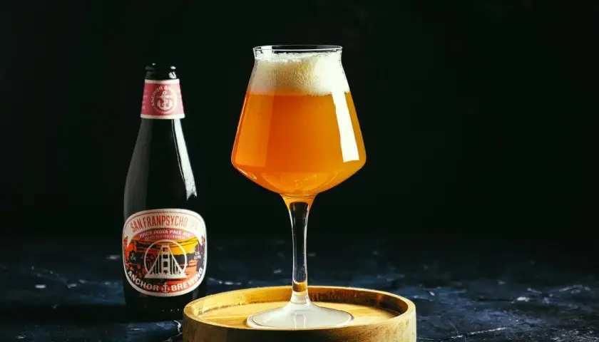 Une bouteille et un verre de bière ambrée Anchor, avec une mousse généreuse. L'étiquette de la bière mentionne "Anchor Brewing".