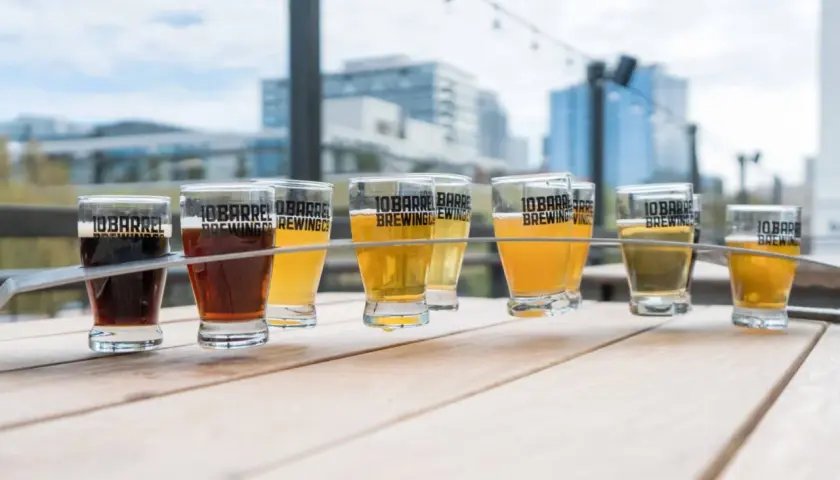 Un assortiment de bières, dont une délicieuse sour ale, sur une table en bois avec des bâtiments en arrière-plan.